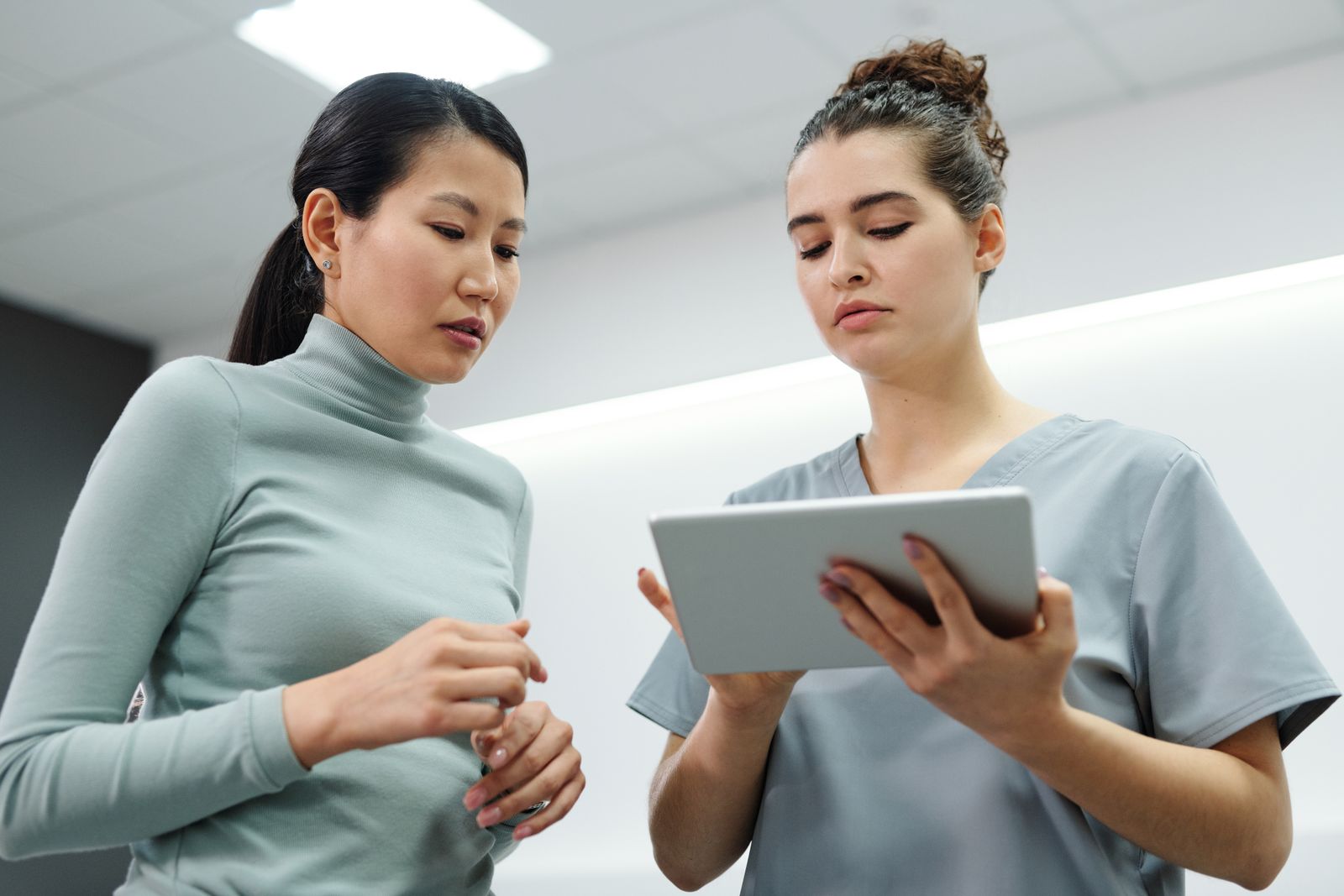 Profesional sanitaria mostrando información en una tablet a una madre, en una clínica luminosa.
